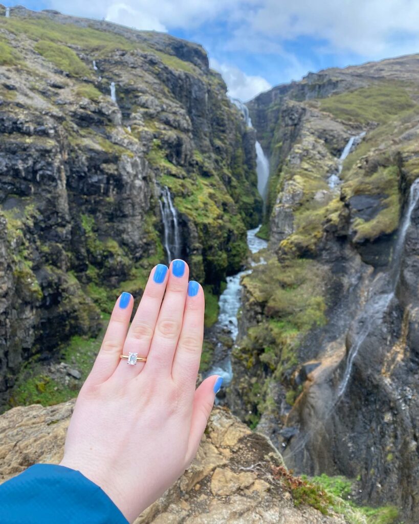 Woman showing off her affordable solitaire engagement ring outside in nature.